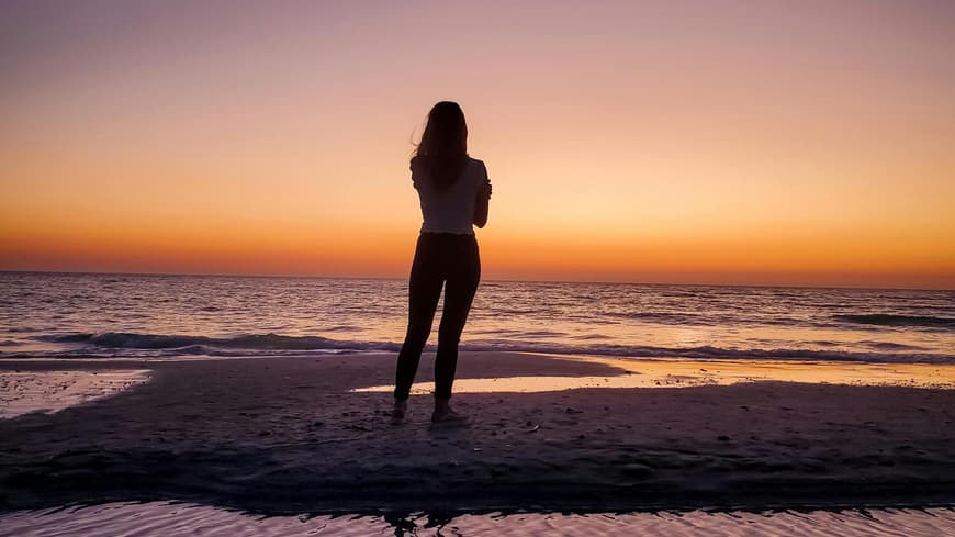 Frau steht beim Sonnenuntergang am Strand