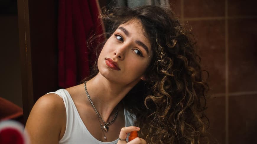 Frau mit Locken sprüht Spray in ihr Haar