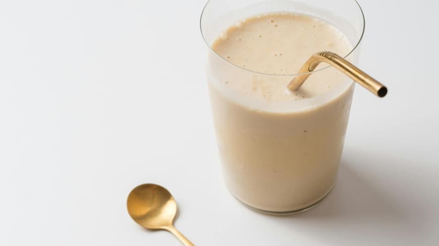 Ein cremiger Shake im Glas mit goldenem Strohhalm.