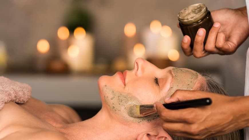 Frau liegt auf dem Rücken und bekommt eine Leinsamen Maske aufs Gesicht geschmiert.