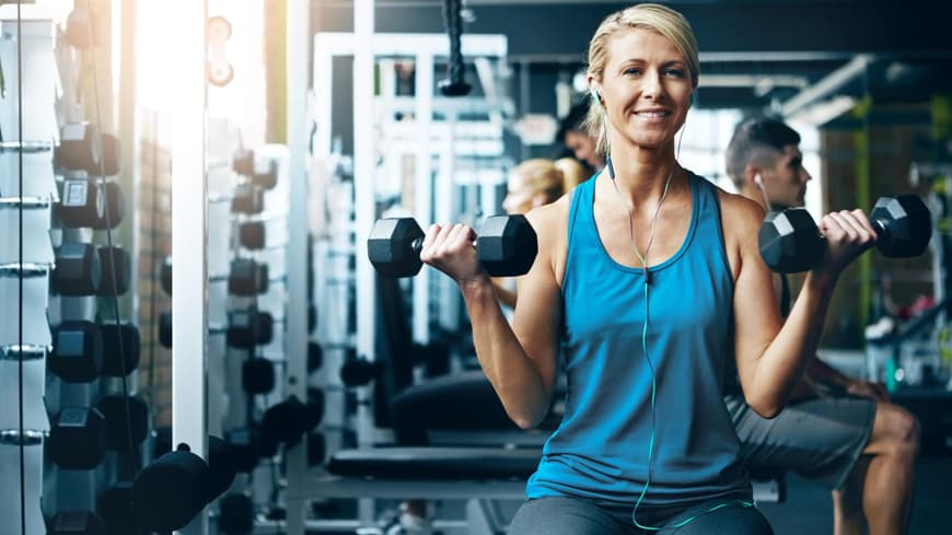 Frau mit zwei Hanteln trainiert ihren Bizeps im Fitnessstudio.