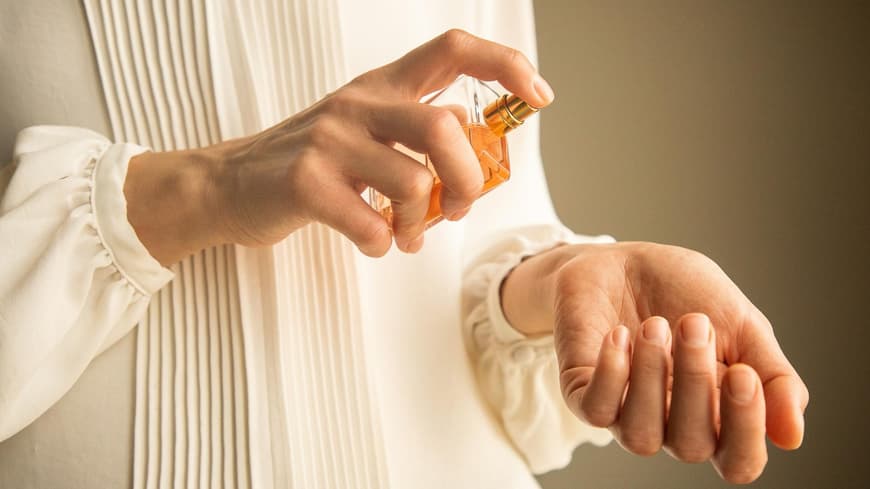 Frau mit einer weißen Bluse hält Parfum Flakon in der Hand.