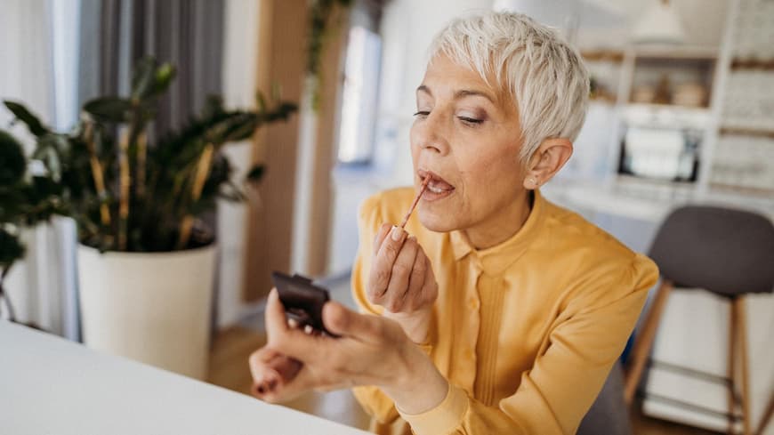 Ältere Frau schminkt sich die Lippen mit einem kleinen Spiegel. 