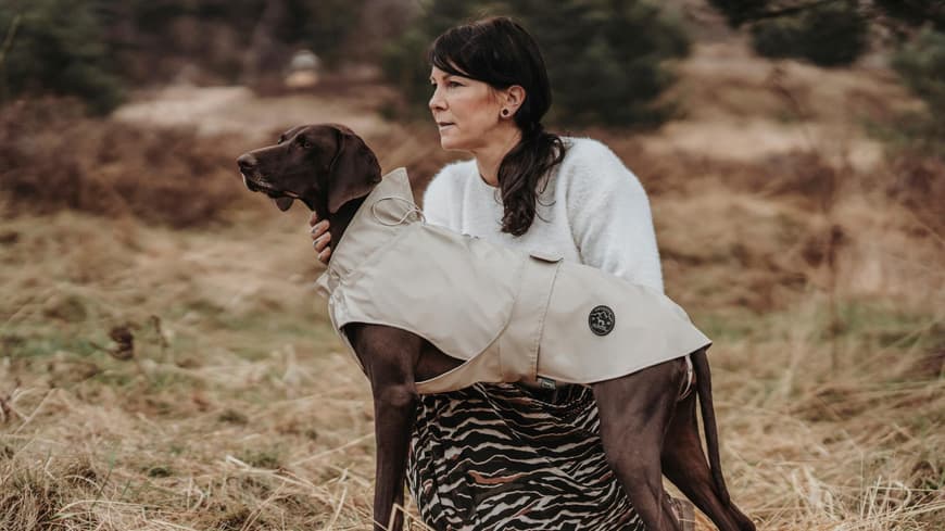 Frau hockt neben einem Hund mit Regenmantel.