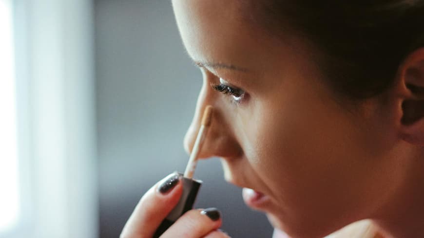 Frau trägt Concealer in ihrem Gesicht auf.