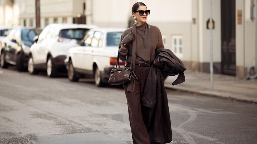 Frau trägt ein komplett braunes Outfit mit Hose, Pullover und Tasche und einer Sonnenbrille.