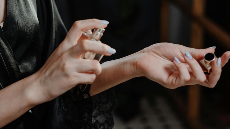 Frau sprüht sich ein Parfum auf das Handgelenk und trägt ein schwarzes Nachthemd.