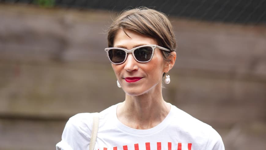 Frau mit braunhaarigem Kurzhaarschnitt, einer beigen Sonnenbrille und roten Lippen.
