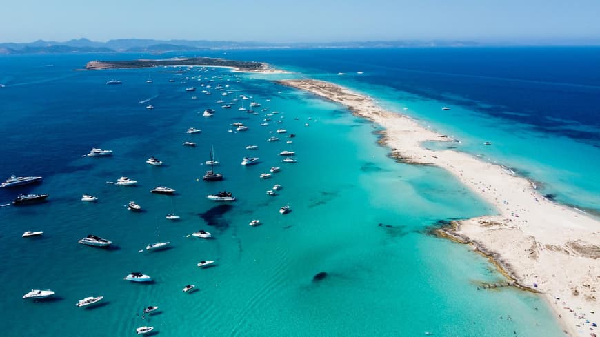Ein langer Sandstrand mit türkisblauem Meer und Yachten darin.