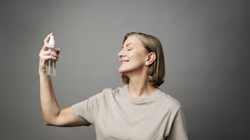 Frau sprüht Gesichtsspray in ihr Gesicht.