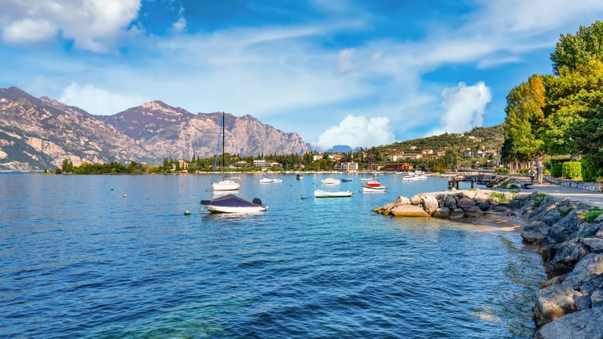 Der Gardasee mit Booten auf dem Wasser und Bergen im Hintergrund.