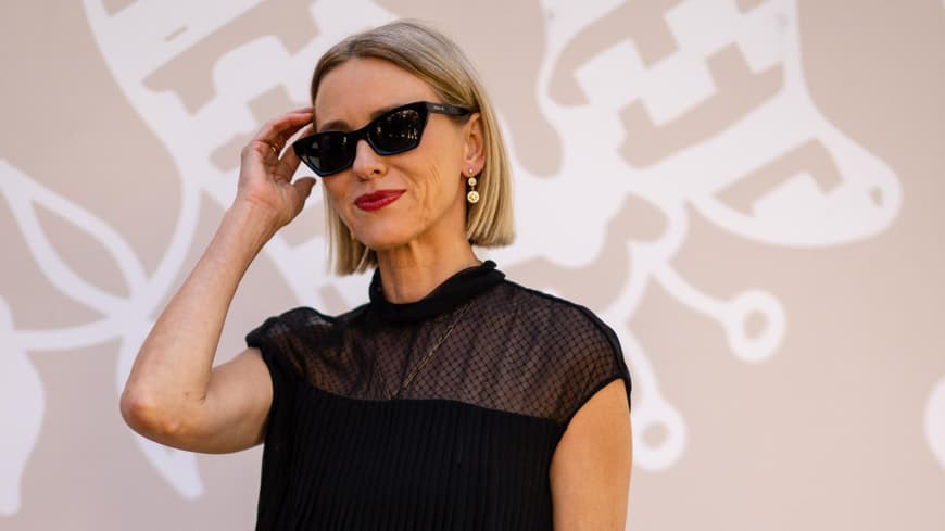 Frau mit kurzen, blonden Haaren, roten Lippen und einer schwarzen Sonnenbrille.
