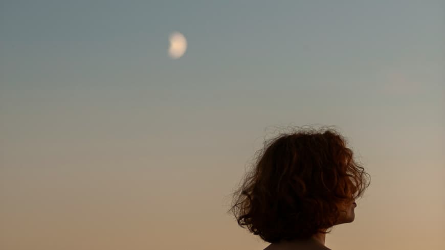 Frau schaut nachdenklich in den Abendhimmel.