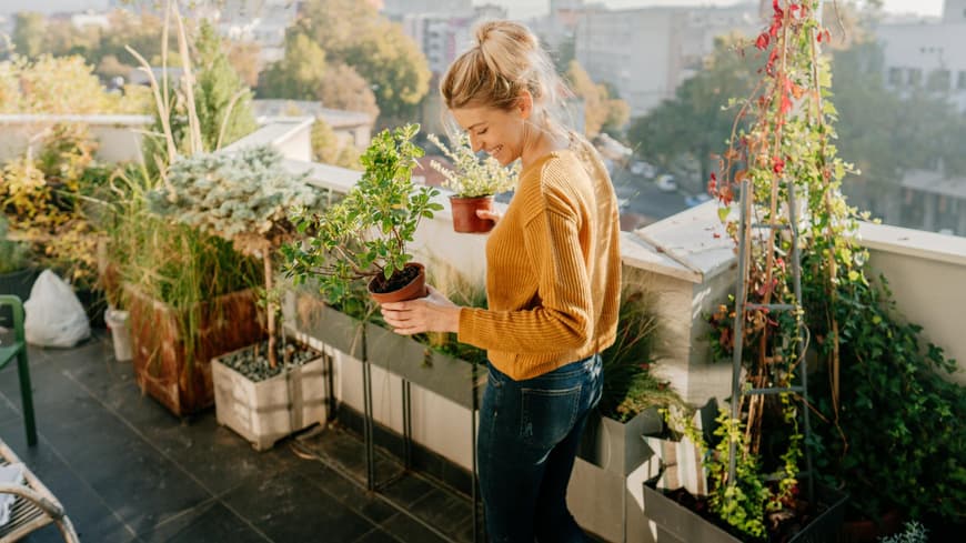 Frau steht auf einem Balkon und hält Pflanzen in der Hand.