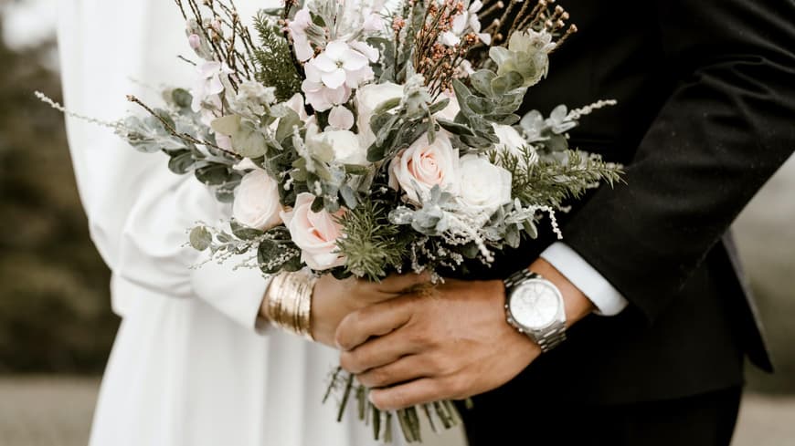 Ein Hochzeitspaar hält gemeinsam den Brautstrauß