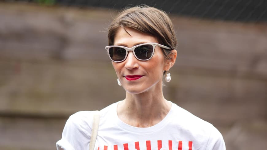Frau mit braunhaarigem Kurzhaarschnitt, einer beigen Sonnenbrille und roten Lippen.