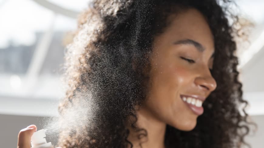 Frau sprüht Spray in die Haare