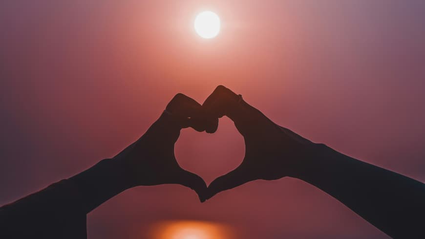 Hände formen ein Herz vor dem Abendhimmel