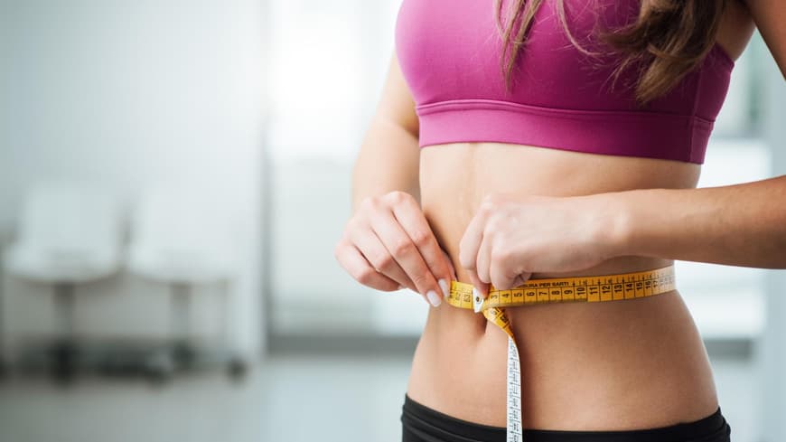 Eine Frau hält ein Maßband um ihre Taille