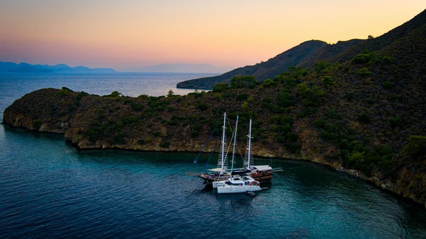 Eine Bucht bei Sonnenaufgang mit einer Gulet und einer Yacht im Wasser.