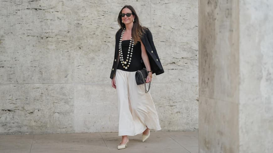 Frau trägt einen weißen Maxi-Rock im Boho-Stil mit einem schwarzen Top und Blazer und zwei großen Perlenketten.