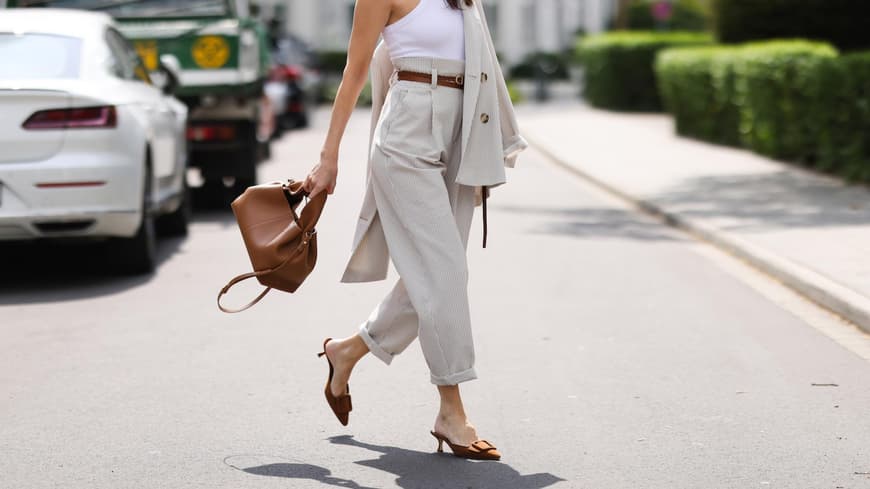 Frau mit rotem Lippenstift trägt ein weißes Top, eine beige Chinohose und Kitten Heals auf der Straße.