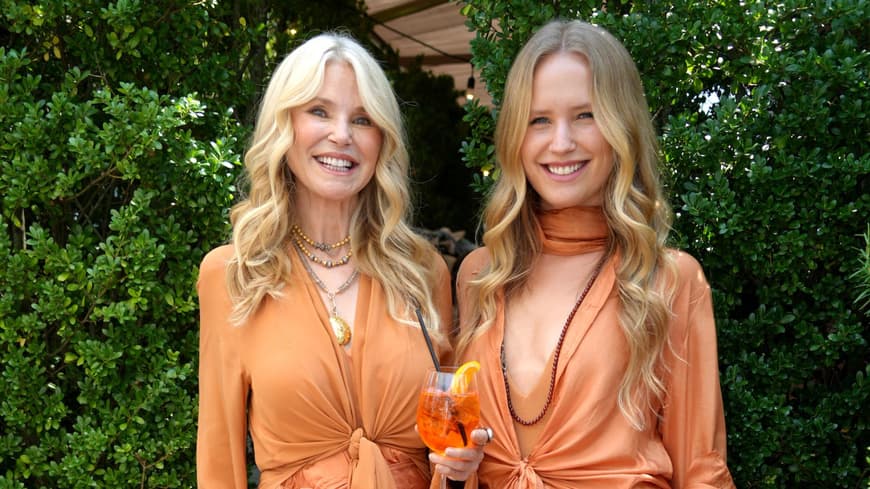 Christie und Sailor Brinkley in orangefarbenen langen Kleidern mit offenen lockigen Haaren und Sandalen.