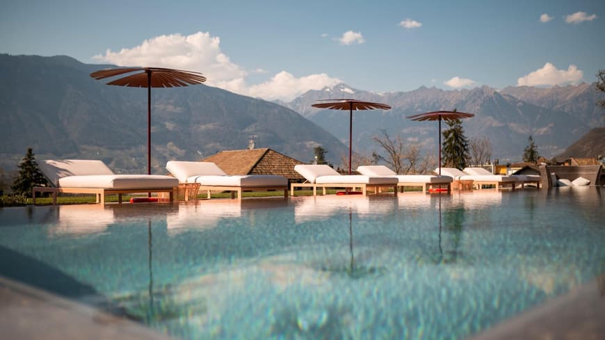 Infinity Pool mit Liegen und Sonnenschirmen und Bergen im Hintergrund.