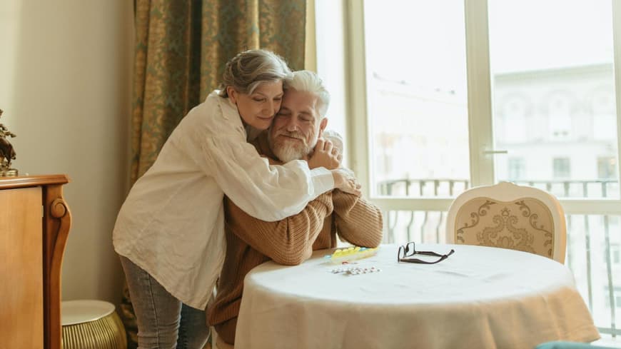 Kuscheln ist besonders zur kalten Jahreszeit eine echte Wohltat für den Körper. Eine Frau umarmt von hinten einen Mann und kuschelt sich an ihn.
