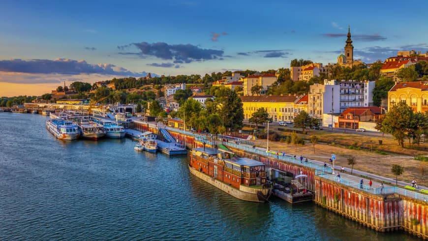 Ein Blick über den Hafen von Belgrad mit Schiffen im Wasser und Häusern an Land, die von der Sonne beleuchtet werden.