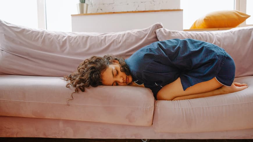 Frau liegt mit Periodenschmerzen auf der Couch