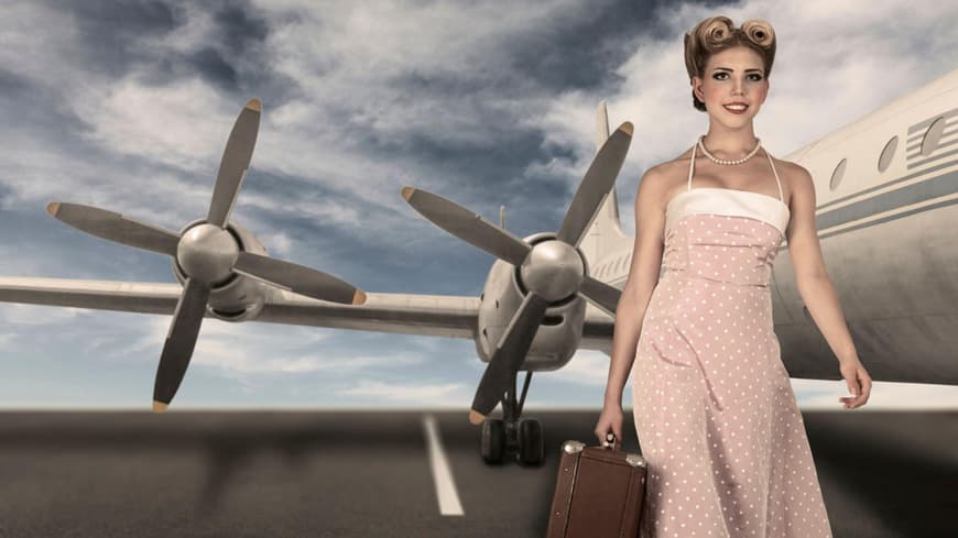 Frau im Sixties-Look mit Koffer vor einem Flugzeug