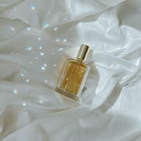 Parfum Flakon liegt auf einem Bettlaken mit Licht und Schatten Parfum Flakon liegt auf einem Bettlaken mit Licht und Schatten