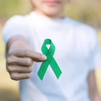 Frau im weißen T-Shirt hält eine grüne Schleife in die Kamera