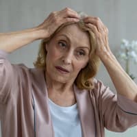 Haarausfall im Herbst ist völlig normal und muss nicht für Unruhe sorgen. Ältere Frau hält die Haare an der Kopfhaut fest.