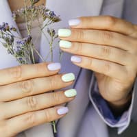 Langanhaltender Nagellack ist für viele Frauen sehr wichtig. Hände mit bunten Fingernägeln und Blumen in der Hand.
