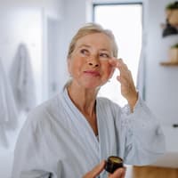 Ältere Frau trägt Augencreme mit Lichtschutzfaktor auf.