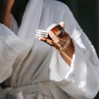 Frau im Bademantel hält eine Cremedose in der Hand. 