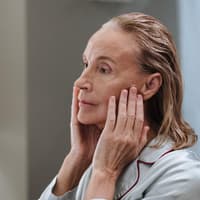 Das beste Serum ab 50 sollte viel Feuchtigkeit spenden. Ältere Frau fasst sich mit den Händen ins Gesicht.