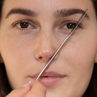 Frau hält sich einen Pinsel am Auge entlang.