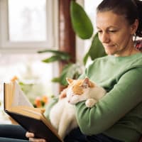 Frau mit Katze auf dem Schoß am Lesen.
