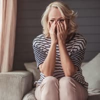 Frau sitzt auf dem Sofa und hält die Hände ins Gesicht.