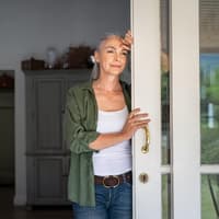 Frau lehnt im Türrahmen und schaut nach draußen.