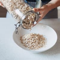 Eine Person schüttet Haferflocken aus einem Glasgefäß in eine Schüssel.