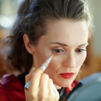 Frau sitzt vor dem Spiegel und deckt ihre Augenringe mit Concealer ab.