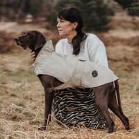 Regenmäntel für Hunde können richtig stylish aussehen. Frau hockt neben einem Hund mit Regenmantel.