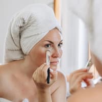 Frau schminkt sich mit einem Pinsel und deckt Augenringe ab.