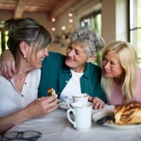 Drei Frauen sitzen am Tisch und sprechen und essen Kuchen.