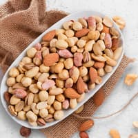 Verschiedene Nüsse in einer weißen Schale, die auf einem braunen Jutebeutel steht.