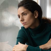 Frau schaut nachdenklich aus dem Fenster